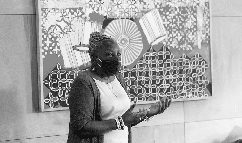 Black and white image of Fela Barclift talking in front of a classroom with a mask on
